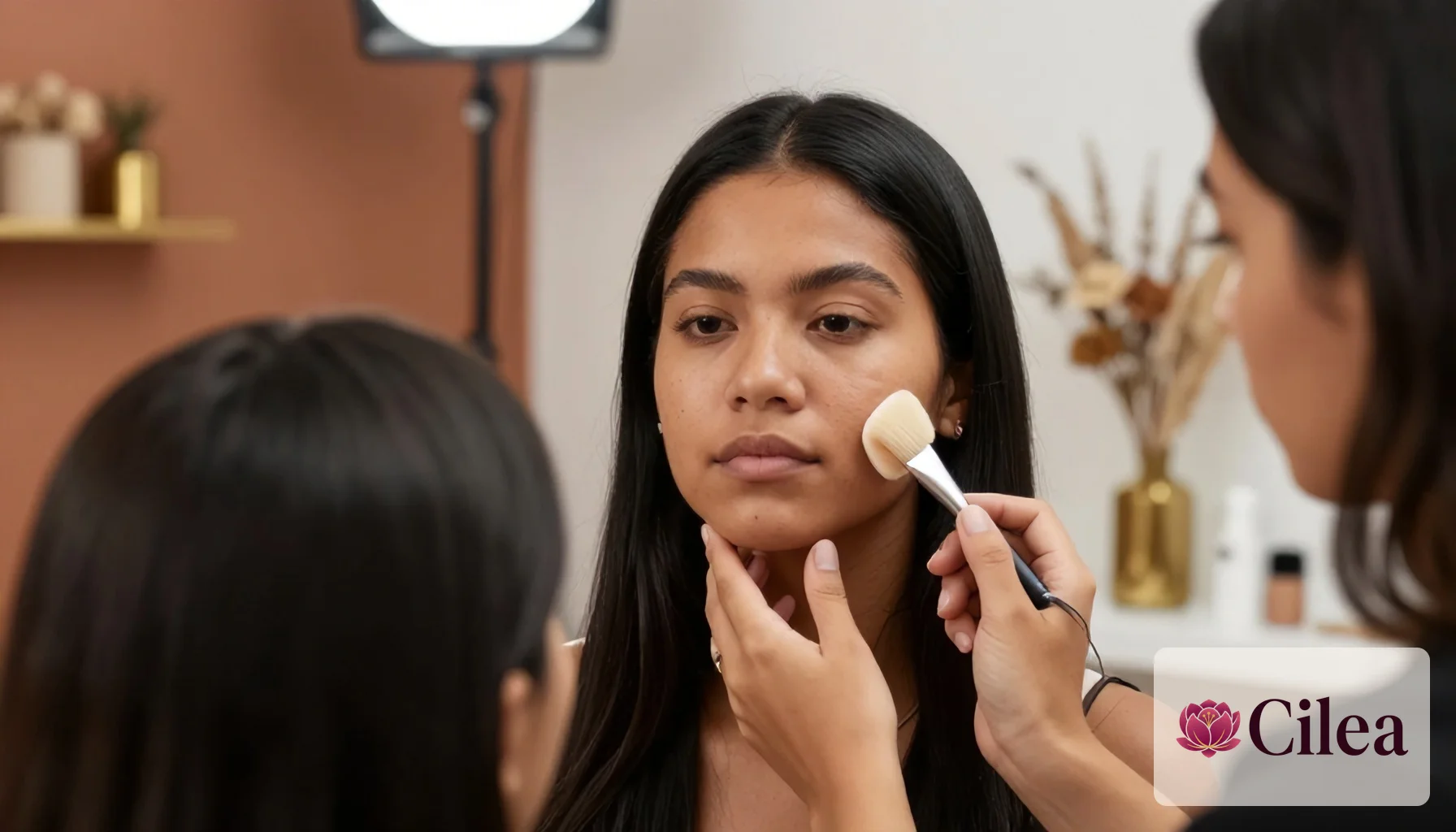 Profissional aplica maquiagem no rosto de cliente em salão de beleza, demonstrando técnica de uso de pincel.